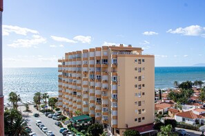 Ein mehrstöckiges Hotel mit Balkonen, einem Parkplatz und Blick aufs Meer.