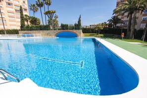 Ein Schwimmbad mit einer Steinbogenbrücke, umgeben von Palmen und einem mehrstöckigen Gebäude.