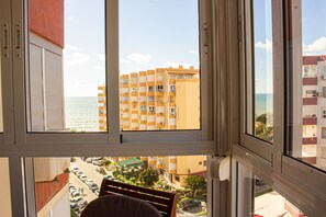 Blick aus einem Fenster auf einen Parkplatz, ein Gebäude mit Balkonen und ein Gewässer.