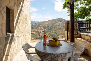 Ein Tisch mit einer Flasche, Gläsern und einer Obstschale auf einer Terrasse mit Blick auf eine hügelige Landschaft.