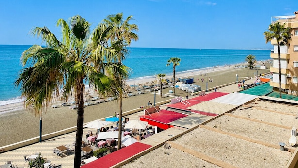 Une vue sur la plage, avec des palmiers, une plage de sable et un bâtiment doté d’un toit rouge.