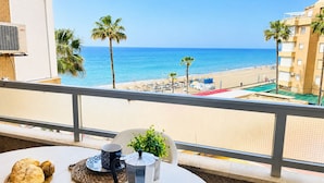 Un balcon donnant sur une plage, une table avec de la nourriture et une cafetière, et un bâtiment avec une enseigne indiquant « RESTAURANT » en arrière-plan.