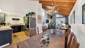 Une cuisine spacieuse avec des poutres en bois, un coin repas doté d’une table en bois et un lustre.