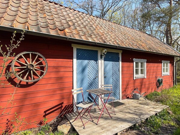 A red wooden house with a blue door, a wheel, and a small table with chairs.