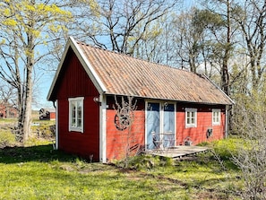 A red wooden house with a sloped roof, a porch, and a wheel in the doorway.