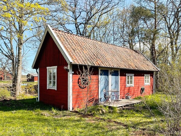 A red wooden house with a sloped roof, a porch, and a wheel in the doorway.