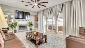 A living room with a fireplace, leather sofas, a coffee table, and a ceiling fan. - Screened Lanai & Yard! Family Getaway in Apopka (Apopka)