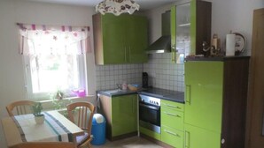 A compact kitchen with green cabinets, a tiled backsplash, a stove, and a dining area with a table and chairs. - in ruhiger Lage in der Nähe zahlreicher Wanderro by Interhome (Wutha)
