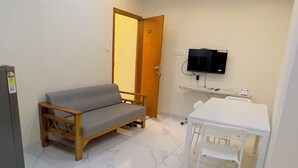 A room with a sofa, a table with chairs, a ceiling fan, a TV, and a refrigerator. - IZEL CASA (Kanayannur)
