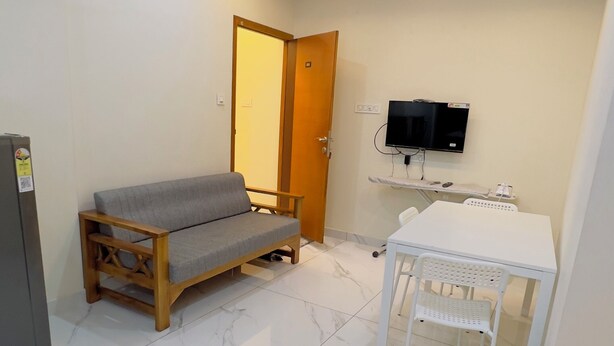 A room with a sofa, a table with chairs, a ceiling fan, a TV, and a refrigerator. - IZEL CASA (Kanayannur)