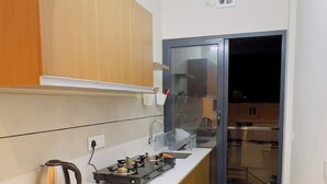 A compact kitchen with wooden cabinets, a gas stove, a kettle, and a green bucket. - IZEL CASA (Kanayannur)