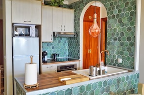 A kitchen with a microwave, oven, and sink, wooden cabinets, a green tiled backsplash, and a hanging light fixture. - Stylish Holiday Apartment in Torrox Park with Sea View (Torrox)