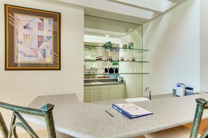 Een moderne keuken met een granieten aanrecht, een lijstwerk abstract schilderij en een glazen kastje met keukengerei.