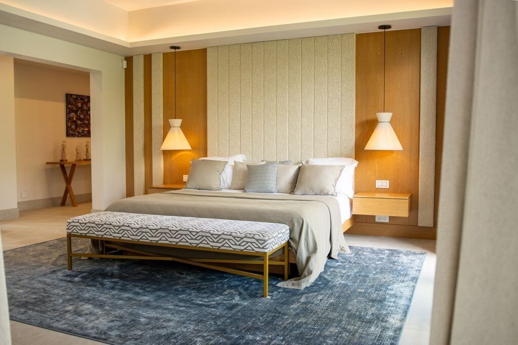 Un dormitorio con cama, lámparas de noche, un banco y una alfombra estampada.