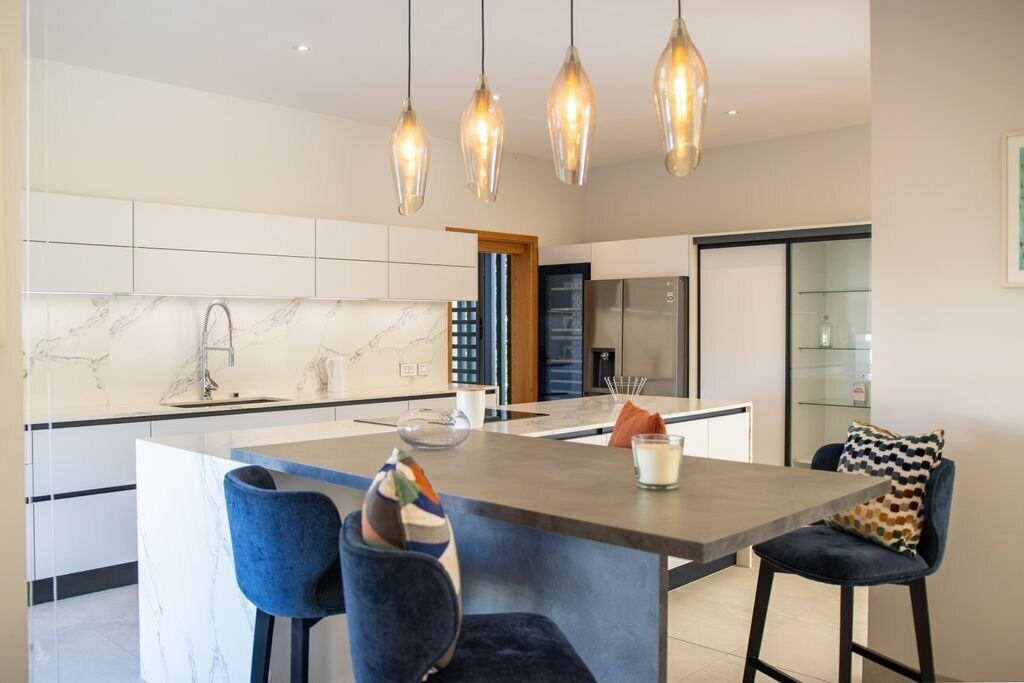 A modern kitchen with a marble backsplash, pendant lights, and a central island with bar stools.