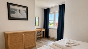 Una camera d'albergo con due letti, una scrivania, una sedia, un mobiletto in vimini e una finestra con tende.