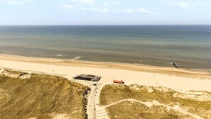 Vista aérea de uma praia com um prédio, uma estrada e dunas.