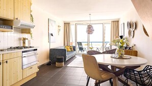 Cozinha moderna com armários de madeira, sala de jantar com mesa redonda e cadeiras, e varanda com área de estar externa.