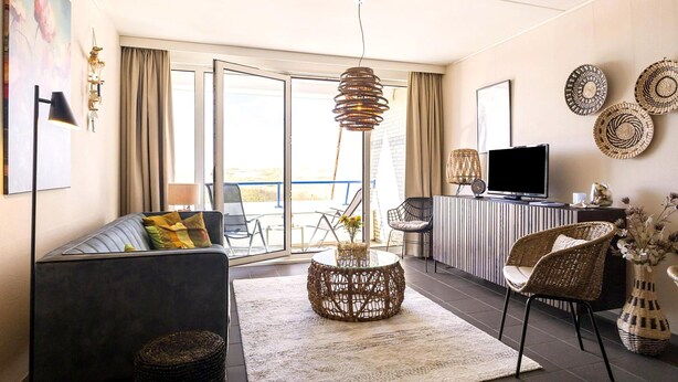 Uma sala de estar moderna com sofá, mesa de centro, televisão e varanda com vista.