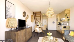 Uma sala de estar moderna com televisão, móveis de vime, um espaço de refeições e uma cozinha.