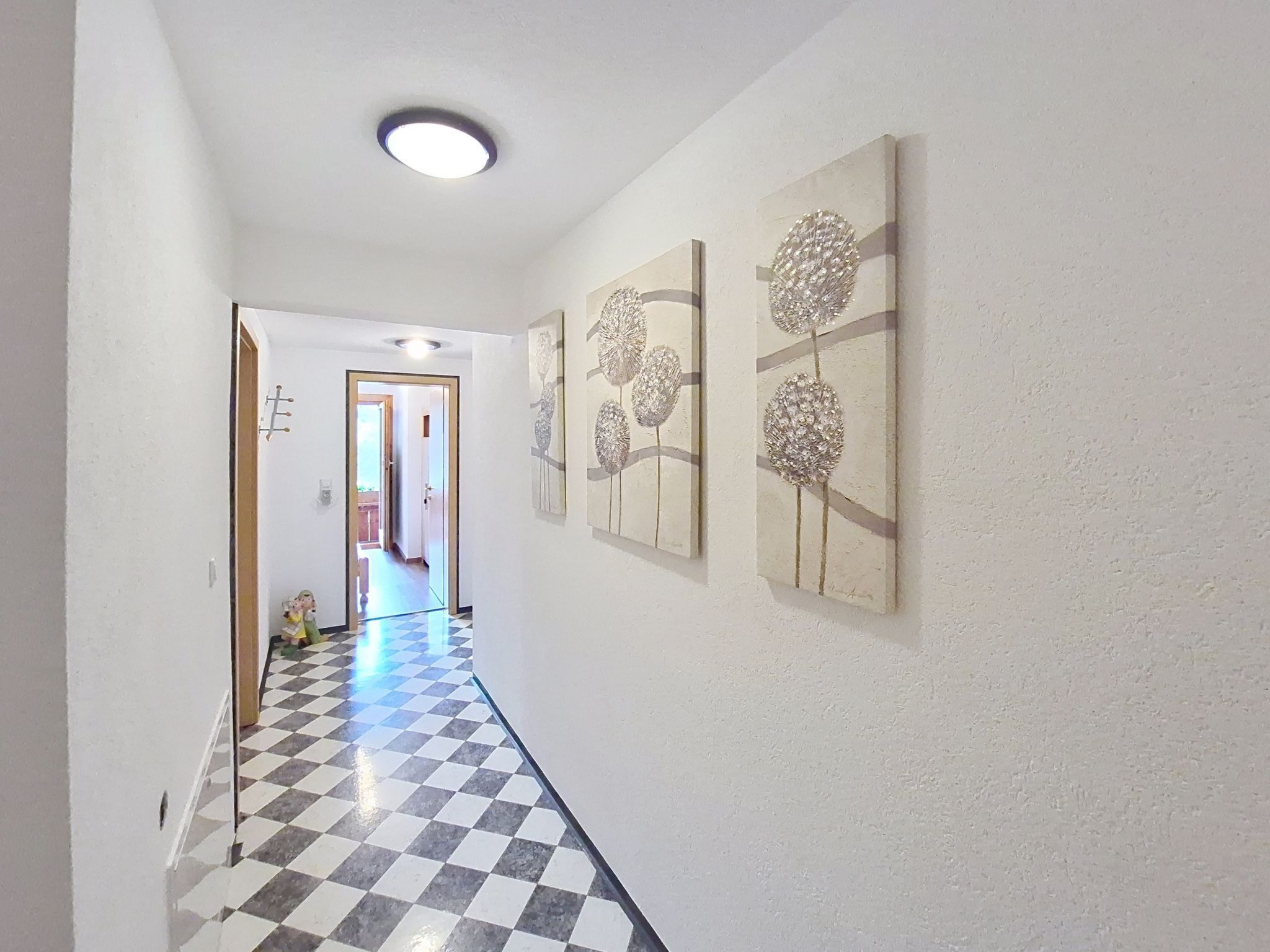 A hallway with a checkered floor, white walls, and three wall-mounted floral paintings.