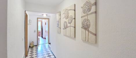 A hallway with a checkered floor, white walls, and three wall-mounted floral paintings.