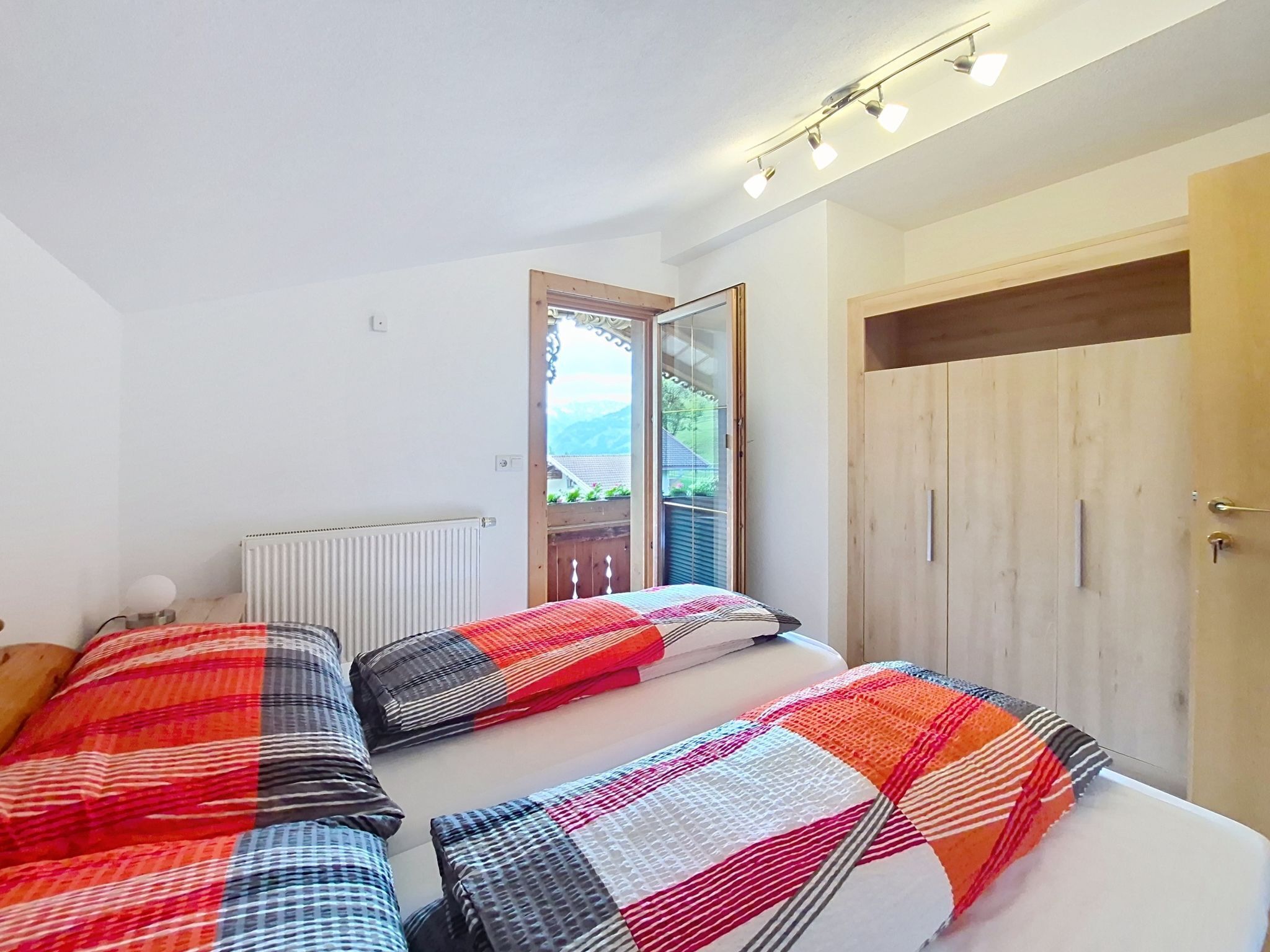A bedroom with a bed, a radiator, a wooden wardrobe, and a window with a view.