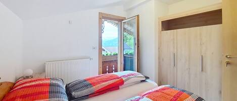 A bedroom with a bed, a radiator, a wooden wardrobe, and a window with a view.
