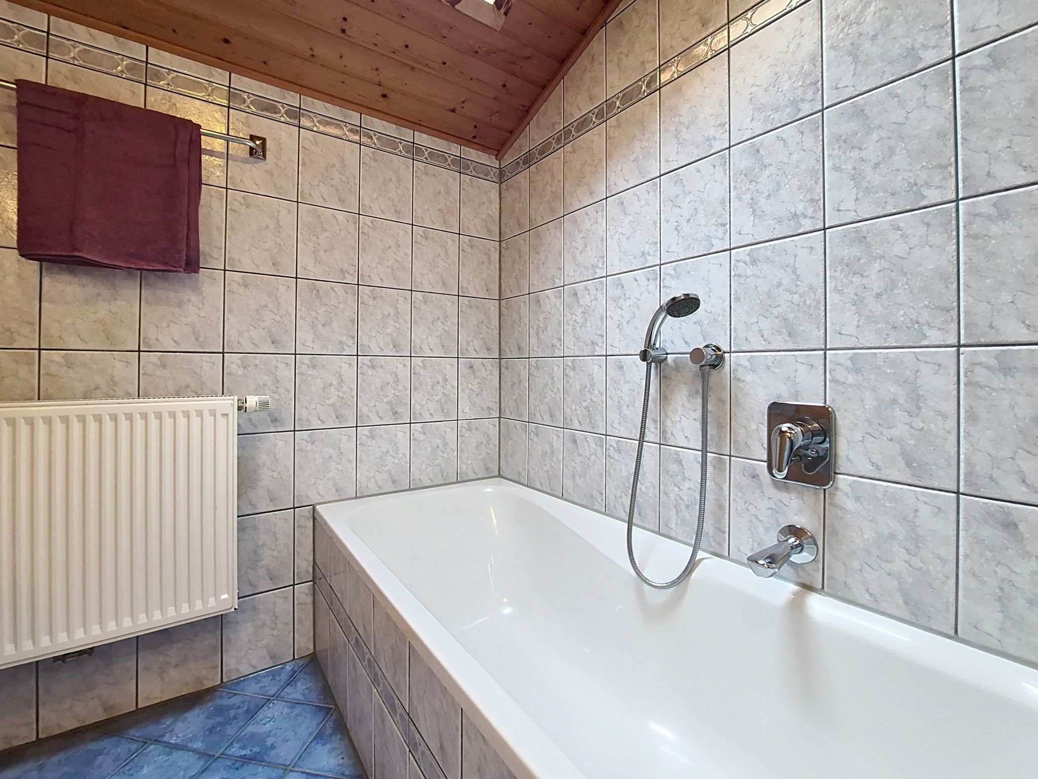 A bathroom with a white bathtub, a showerhead, and a towel hanging on the wall.
