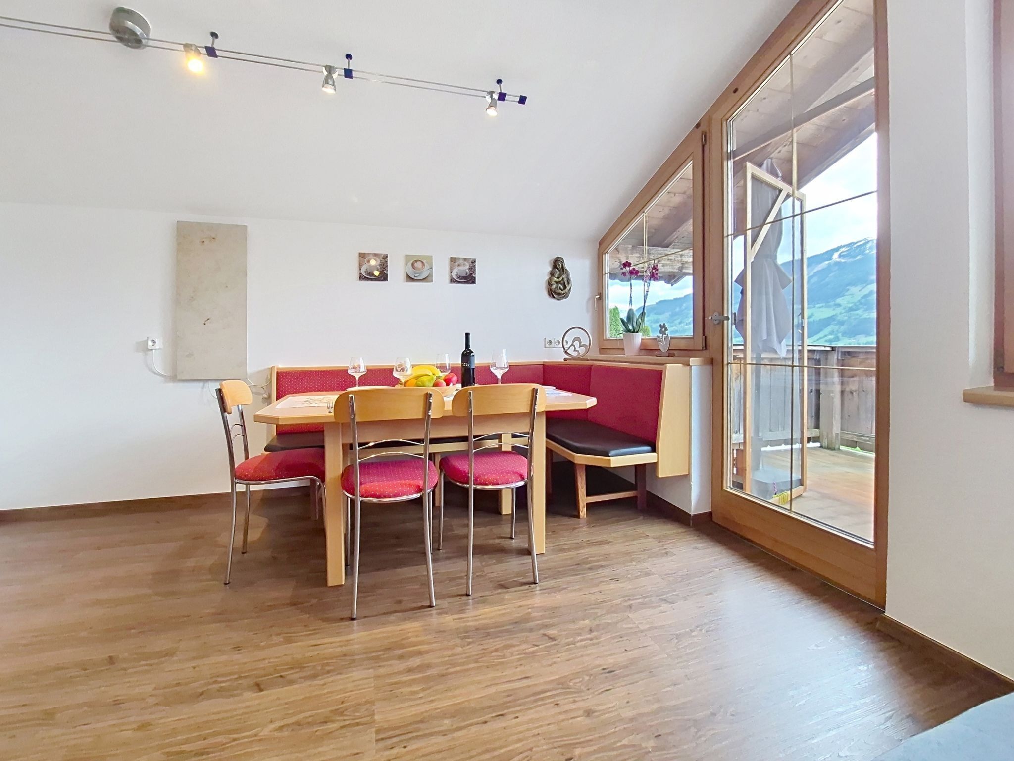 A dining area with a wooden table and red cushioned chairs, a red bench, and a large window with a mountain view.
