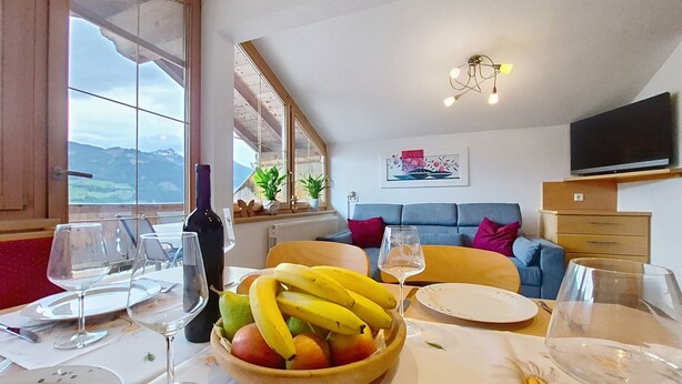 Et spiseområde med et bord dækket til to personer, en skål med frugt, vinglas og en vinflaske.