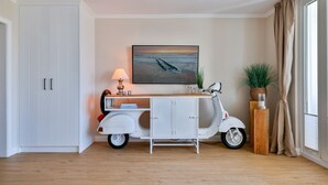 A room with a white cabinet, a scooter, a painting, and a plant. - Dünenglück No. 4 - The vacation apartment Dünenglück No. 4 on the beach for max. 4 (Sylt)