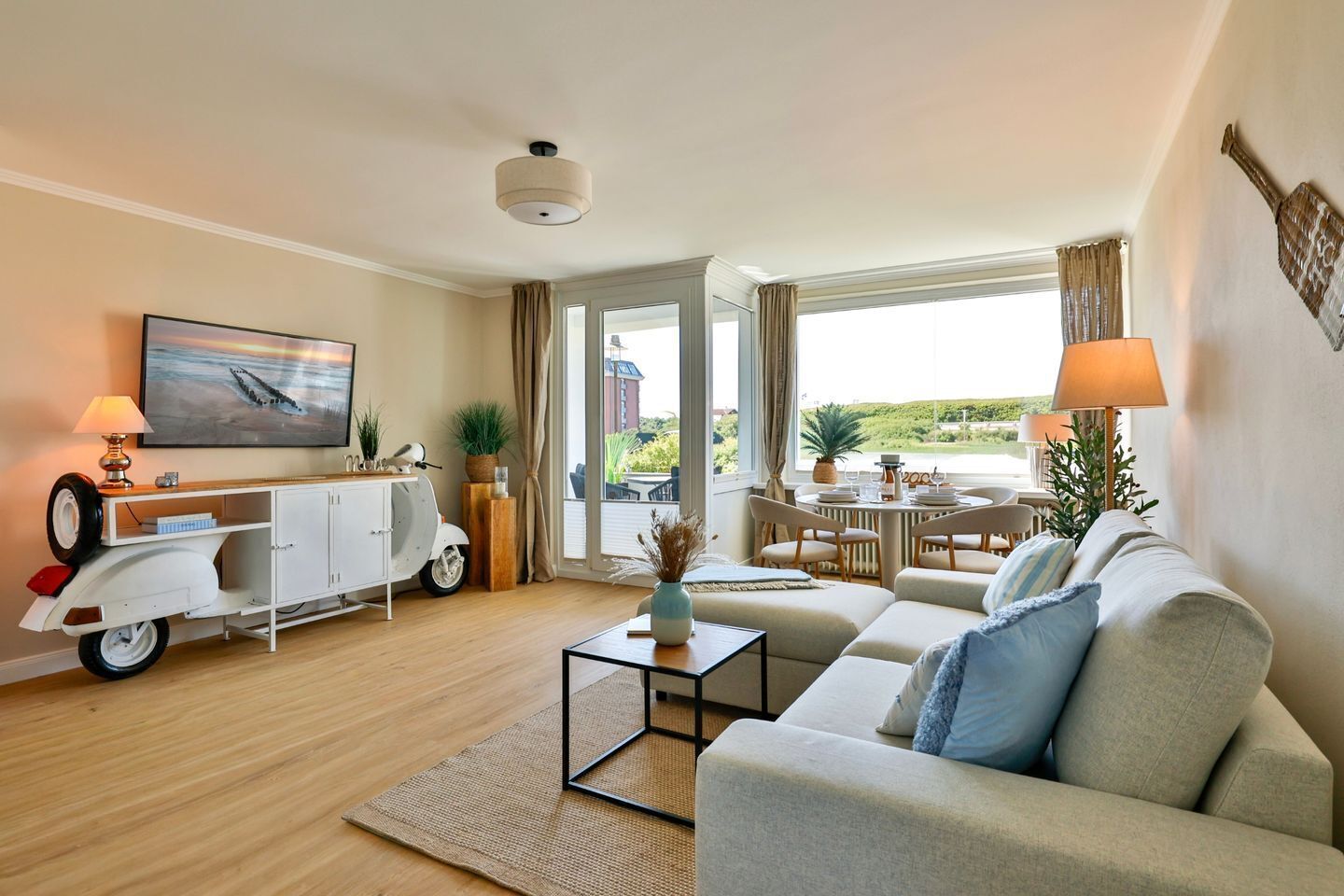A living room with a sofa, a coffee table, a TV, a dining area with chairs, and a view through the window.