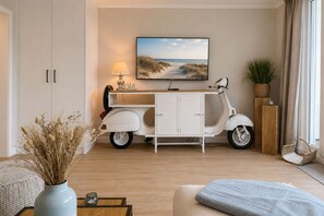 En stue med en hvid sofa, et lille bord med en vase, en scooter, et skab, en lampe, et indrammet billede og en plante.