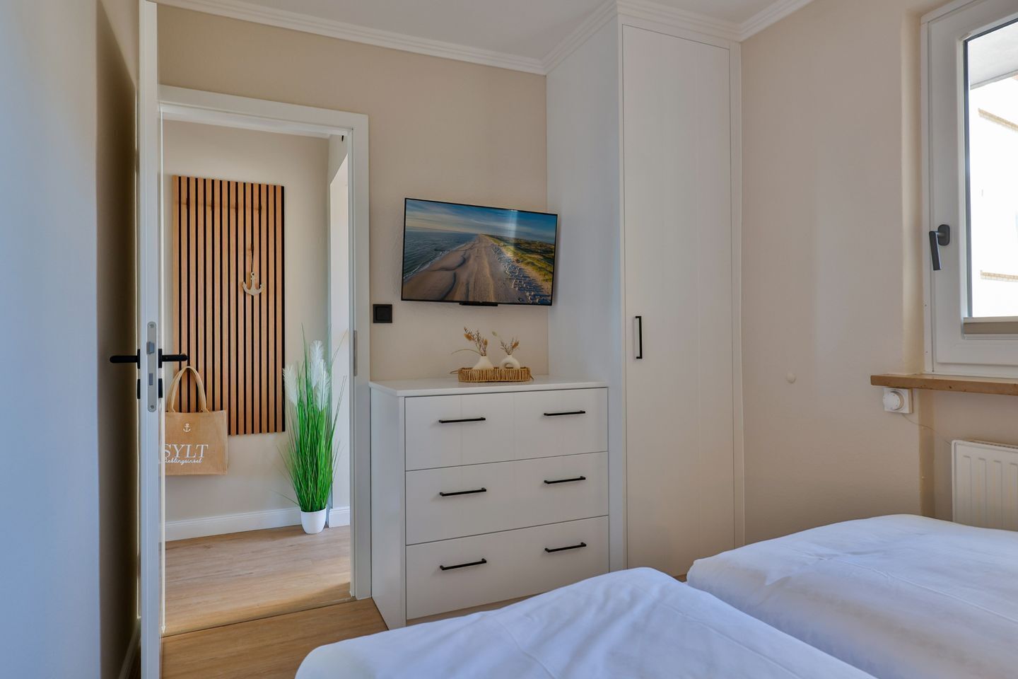 Une chambre à coucher avec un lit, une commode, un tableau et une plante en pot.