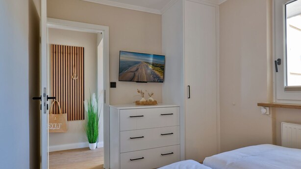 A bedroom with a bed, a dresser, a painting, and a potted plant. - Dünenglück No. 4 - The vacation apartment Dünenglück No. 4 on the beach for max. 4 (Sylt)