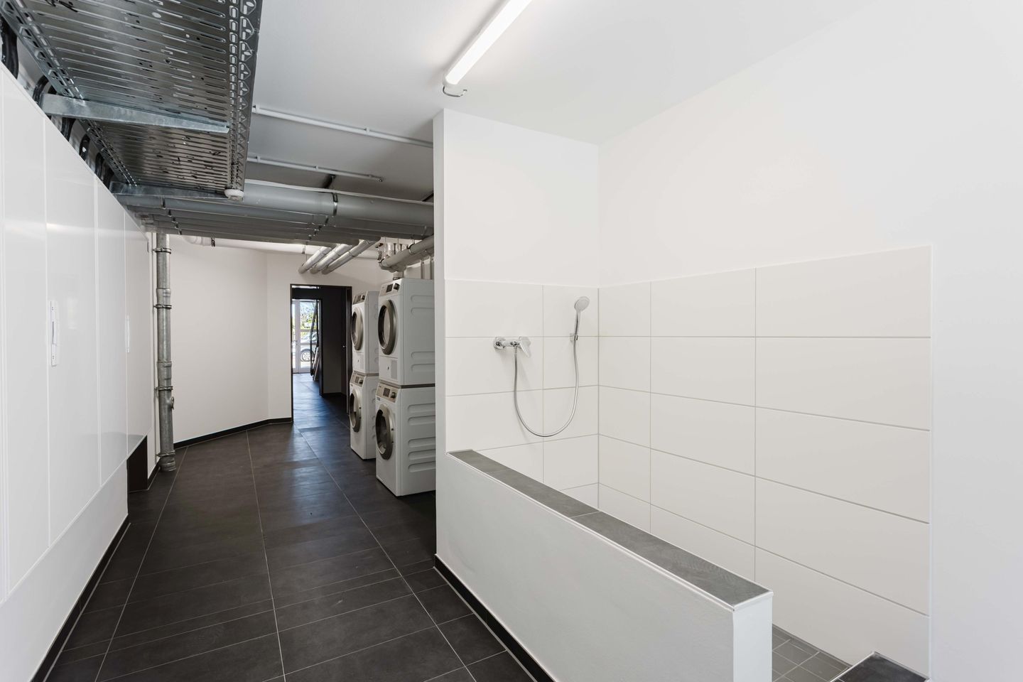A laundry room with stacked washers and dryers, a shower, and a ventilation system.