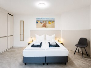 Ein Hotelzimmer mit einem Bett, Nachttischlampen, einem Sessel, einem Gemälde und einem Kleiderschrank.