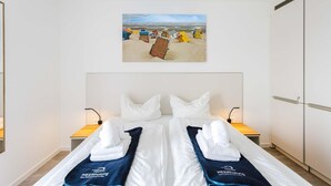 A hotel room with a bed, two bedside tables, a wall-mounted artwork of a beach scene, and a wardrobe. - MEERholung Vacation Rental 3.9 with Ocean View, Balcony, and Sleeps 4 - MEERholung House (Cuxhaven)