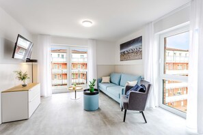 Ein modernes Wohnzimmer mit einer Couch, einem Sessel, einem Couchtisch, einem Fernseher und einem Fenster mit Blick auf Gebäude.