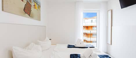 Une chambre d’hôtel avec un lit, un tableau, une télévision et une fenêtre donnant sur des immeubles.