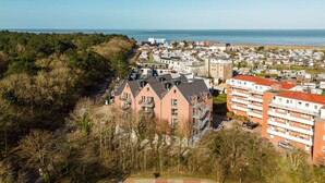 A coastal residential area with modern apartment buildings, a beach in the background, and a dense forested area. - MEERholung Vacation Rental 3.6 with Balcony for up to 5 Guests, 400 m from the Sea - House (Cuxhaven)