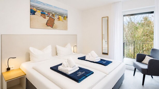 A hotel room with a large bed, a nightstand, a chair, a balcony with a view, and a painting on the wall. - MEERholung Vacation Rental 3.6 with Balcony for up to 5 Guests, 400 m from the Sea - House (Cuxhaven)