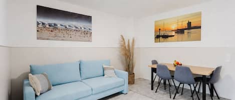Una habitación con un sofá azul claro, una mesa de comedor con cuatro sillas y dos cuadros en las paredes.