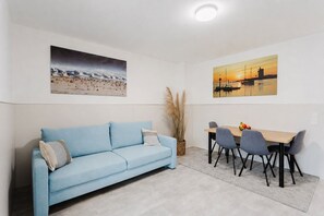 Ein Zimmer mit einem hellblauen Sofa, einem Esstisch mit vier Stühlen und zwei Bildern an den Wänden.