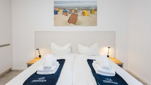 A hotel room with a bed, two bedside tables, a wall-mounted picture of beach chairs, and a white door. - MEERholung Vacation Rental 3.6 with Balcony for up to 5 Guests, 400 m from the Sea - House (Cuxhaven)