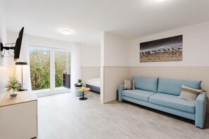 A modern living room with a light blue sofa, a small round table, and a TV mounted on the wall. - MEERholung Vacation Rental 3.6 with Balcony for up to 5 Guests, 400 m from the Sea - House (Cuxhaven)