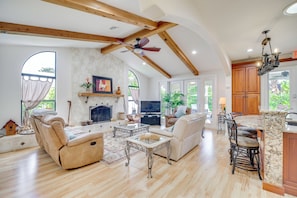 A spacious living room with a fireplace, a ceiling fan, and a kitchen area with wooden cabinets and a marble countertop.