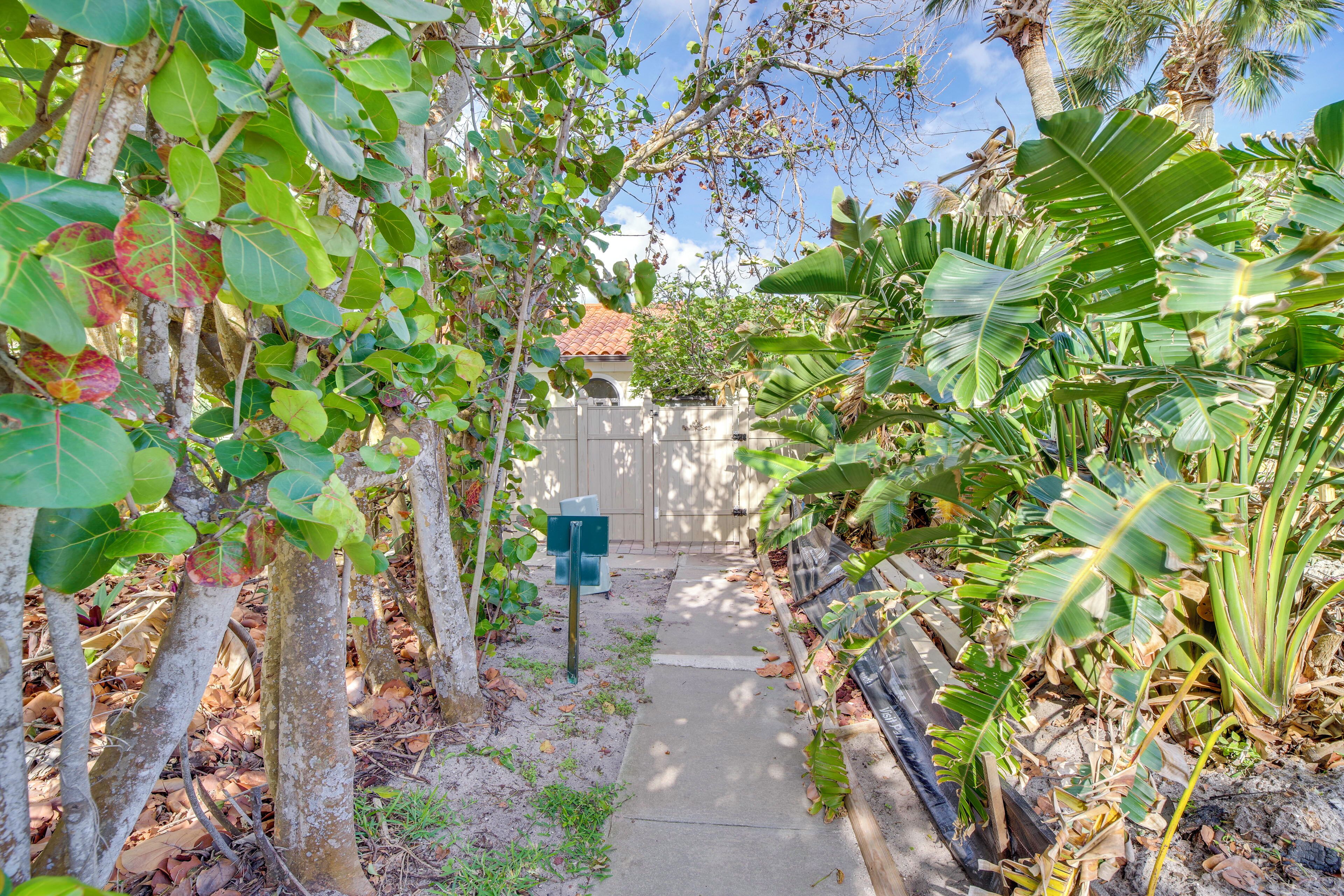 A narrow pathway flanked by lush greenery and a building with a tiled roof.