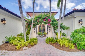 A pathway leading to a building with a tiled roof, surrounded by palm trees and flowering plants.